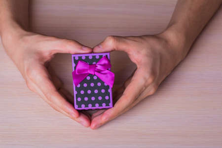 Two male hands in shape of heart holding purple spotted gift box.の写真素材