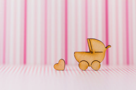 Wooden icon of baby carriage and little heart on pink striped background.の写真素材