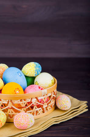 Colorful Easter eggs in wicker basket on textile on dark wooden background.の写真素材