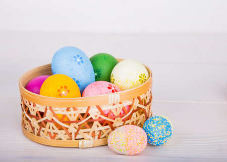 Colorful Easter eggs in wicker basket on white wooden background.の写真素材