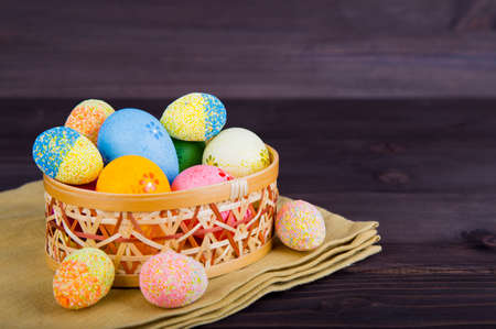 Colorful Easter eggs in wicker basket on textile on dark wooden background.の写真素材