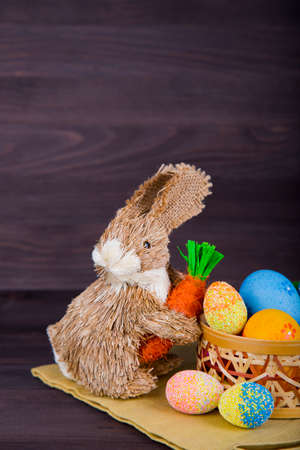 Wicker Easter bunny with Easter eggs in basket on dark wooden background.の写真素材