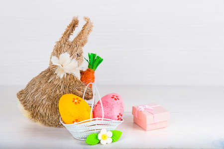 Wicker Easter bunny with Easter eggs in basket on white wooden background and pink gift boxの写真素材