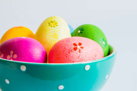Colorful easter eggs in green spotted bowl on light background.の写真素材
