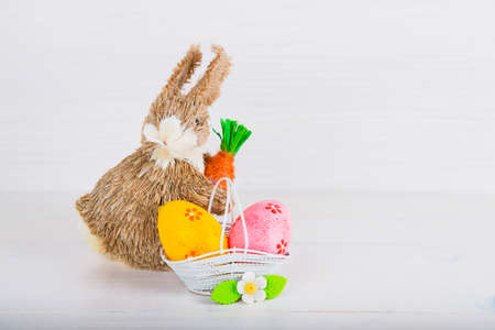 Wicker Easter bunny with Easter eggs in basket on white wooden background.の写真素材