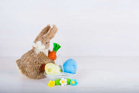 Wicker Easter bunny with Easter eggs in basket on white wooden background.の写真素材