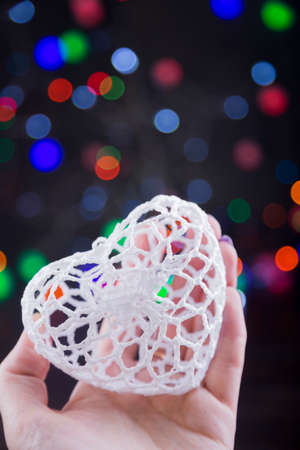 Knitted white heart in hand with garland lights on colorful bokeh background.の写真素材