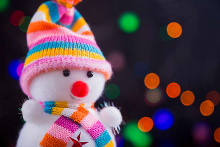 Toy cute snowman with garland lights on colorful bokeh background close-up.の写真素材