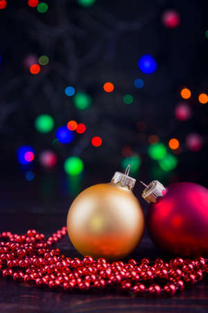 Red and golden Christmas balls and beads with garland lights on colorful bokeh background.の写真素材