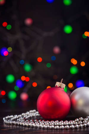 Red and silver Christmas balls and beads with garland lights on colorful bokeh background.の写真素材
