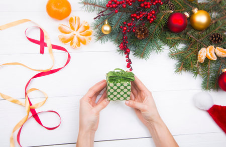 Hands holding green gift box on Christmas decorations background.