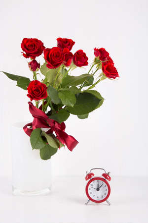 Bouquet of red roses with red alarm clock on white background.の写真素材