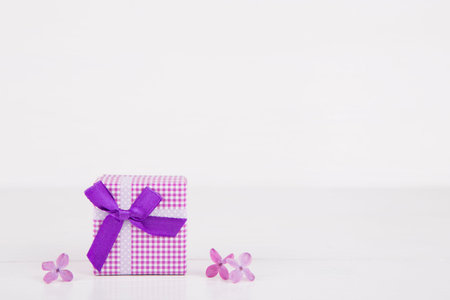 Purple gift box surrounded by lilac flowers on white background.