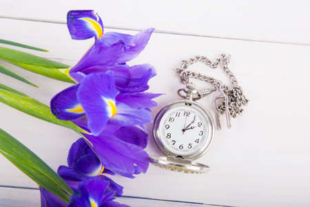 Bouquet of irises with alarm clock on white wooden background.の写真素材