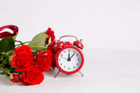Bouquet of red roses with red alarm clock on white background.の写真素材