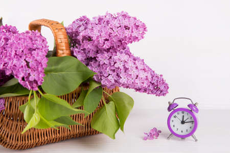 Bouquet of lilac in wicker basket with purple alarm clock on white background.の写真素材