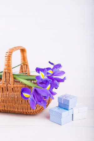 Bouquet of irises in basket with gift boxes on white wooden background.の写真素材