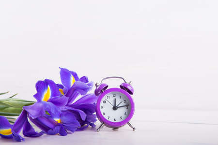 Bouquet of irises with alarm clock on white wooden background.の写真素材