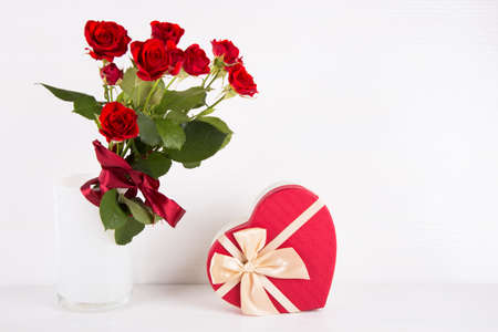 Bouquet of red roses with heart-shaped gift box on white background.の写真素材