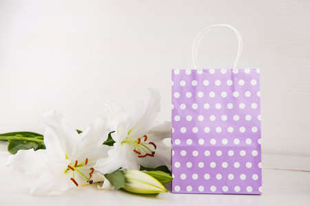 Lilac paper shopping bag with bouquet of white lilies on white background.の写真素材