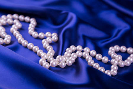 Pearl necklace on dark blue curvy satin fabric.の写真素材