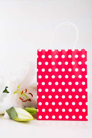 Red paper shopping bag with bouquet of white lilies on white background.の写真素材