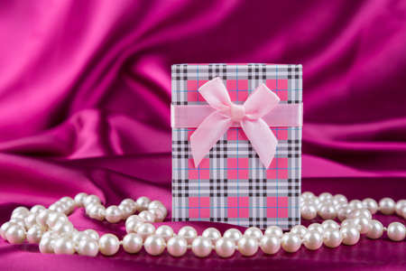 Gift box on curvy satin fabric background with pearl necklace.の写真素材