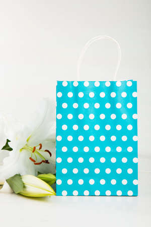 Blue paper shopping bag with bouquet of white lilies on white background.の写真素材