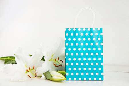 Blue paper shopping bag with bouquet of white lilies on white background.の写真素材