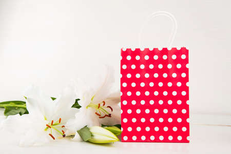 Red paper shopping bag with bouquet of white lilies on white background.の写真素材