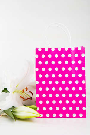 Pink paper shopping bag with bouquet of white lilies on white background.の写真素材