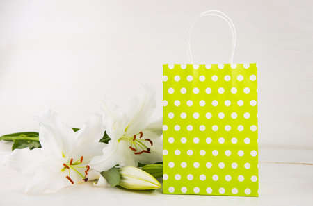 Green paper shopping bag with bouquet of white lilies on white background.の写真素材