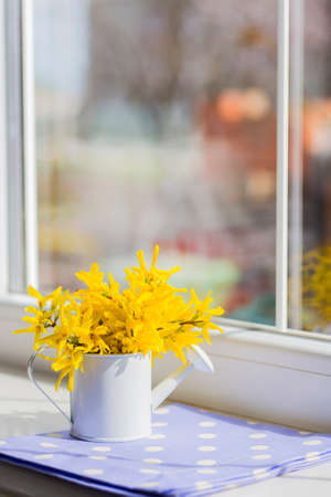Little white watering can with spring flowers bouquet near the windowの写真素材