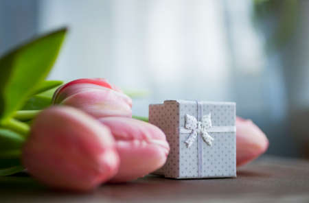 Bouquet of pink tulips with white gift box on table.の写真素材