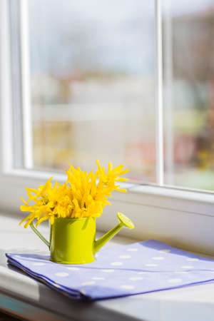 Little green watering can with spring flowers bouquet near the windowの写真素材