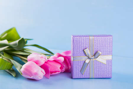 Bouquet of tender pink tulips with lilac gift box on light blue wooden backgroundの写真素材