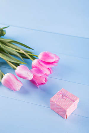 Bouquet of tender pink tulips with pink gift box on light blue wooden backgroundの写真素材