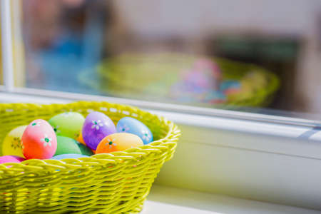 Mix of colorful easter eggs in wicker basket near window.の写真素材