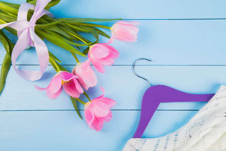 Bouquet of tender pink tulips and hanger with clothes on blue wooden background.の写真素材