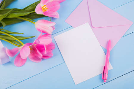 Bouquet of tender pink tulips with empty paper sheet and envelope on blue wooden backgroundの写真素材