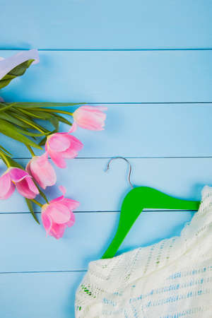 Bouquet of tender pink tulips and hanger with clothes on blue wooden background.の写真素材