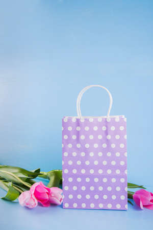 Lilac shopping bag with bouquet of pink tulips on blue wooden background.の写真素材