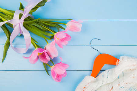 Bouquet of tender pink tulips and hanger with clothes on blue wooden background.の写真素材