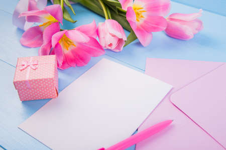 Bouquet of tender pink tulips with empty paper sheet, envelope and gift box on blue wooden backgroundの写真素材