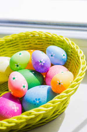 Mix of colorful easter eggs in wicker basket near window.の写真素材