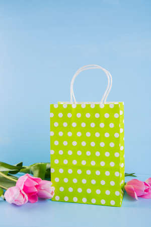 Green shopping bag with bouquet of pink tulips on blue wooden background.の写真素材