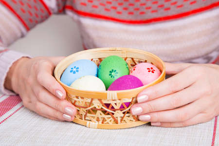 Female hands holding wicker basket with colored easter eggs.の写真素材