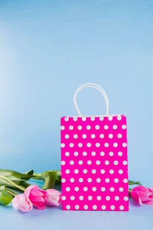 Crimson shopping bag with bouquet of pink tulips on blue wooden background.の写真素材
