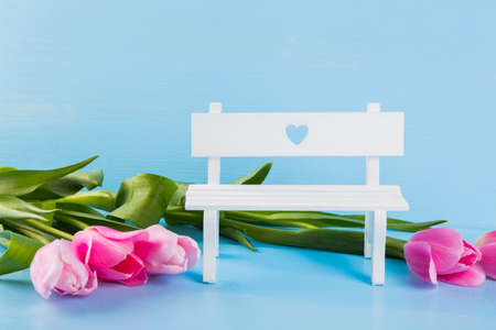 Bouquet of tender pink tulips with white bench on blue wooden background.の写真素材