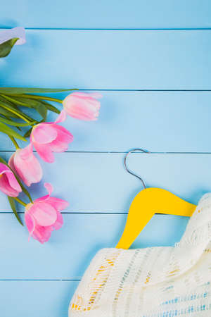 Bouquet of tender pink tulips and hanger with clothes on blue wooden background.の写真素材